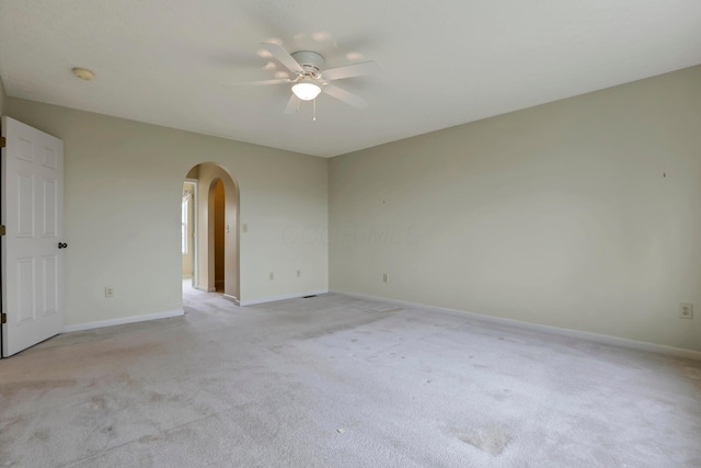 empty room featuring light carpet, arched walkways, baseboards, and a ceiling fan