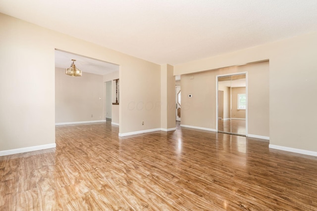 unfurnished room featuring baseboards, an inviting chandelier, and wood finished floors