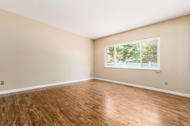empty room with baseboards, visible vents, and wood finished floors