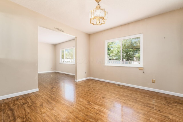 unfurnished room featuring visible vents, baseboards, wood finished floors, and a chandelier