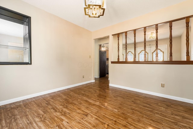 empty room with baseboards, wood finished floors, and a notable chandelier
