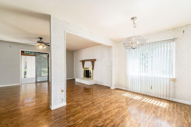 unfurnished living room with a fireplace, ceiling fan with notable chandelier, baseboards, wood finished floors, and visible vents