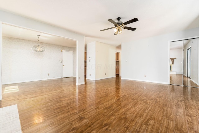unfurnished living room with baseboards, ceiling fan with notable chandelier, and wood finished floors