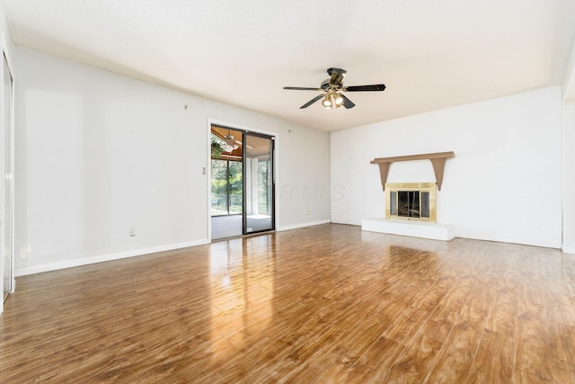 unfurnished living room featuring baseboards, a glass covered fireplace, ceiling fan, and wood finished floors