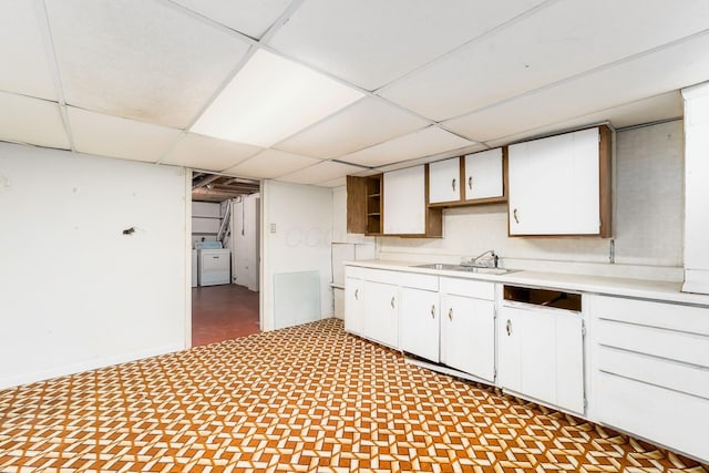 kitchen featuring a paneled ceiling, a sink, light countertops, washer / dryer, and white cabinetry