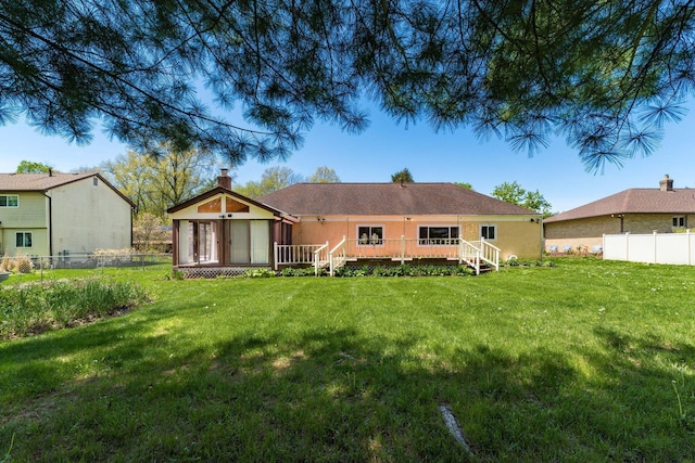 rear view of house with a wooden deck, a yard, a chimney, and fence