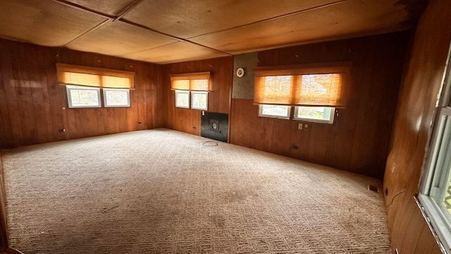 unfurnished room featuring visible vents, wooden walls, and carpet floors