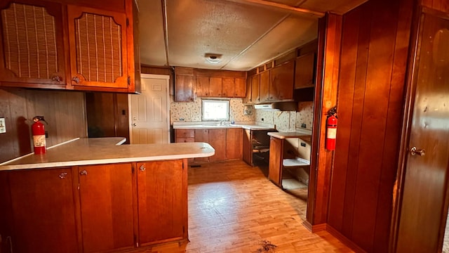 kitchen with brown cabinets, light countertops, light wood-style flooring, and a peninsula