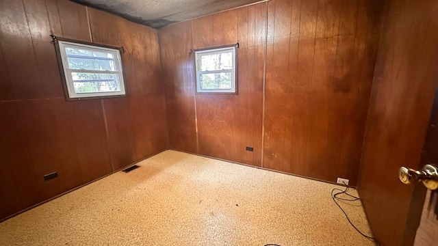 unfurnished room featuring visible vents, wood walls, and a healthy amount of sunlight