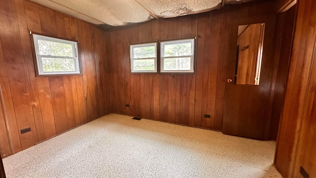 carpeted spare room with visible vents, wood walls, and a textured ceiling
