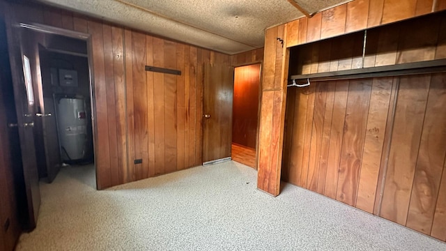 unfurnished bedroom with water heater, wooden walls, carpet floors, and a textured ceiling