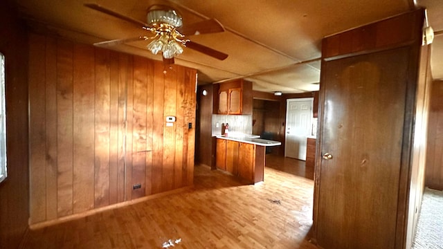 kitchen featuring wood walls, a peninsula, brown cabinets, a ceiling fan, and light wood-style floors