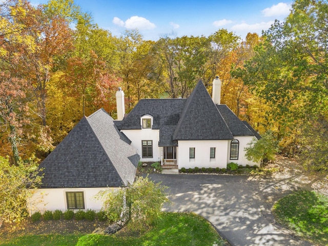 view of front facade with a chimney, stucco siding, roof with shingles, and aphalt driveway