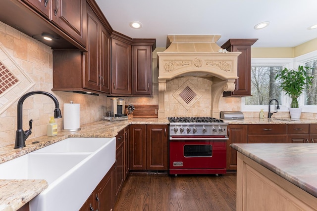 kitchen featuring dark wood finished floors, stainless steel range, a sink, light stone countertops, and custom exhaust hood