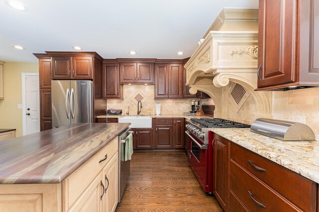 kitchen with dark wood-style flooring, stainless steel appliances, backsplash, a sink, and light stone counters