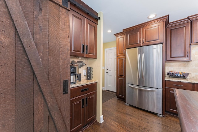 kitchen with dark wood finished floors, tasteful backsplash, light stone countertops, and freestanding refrigerator