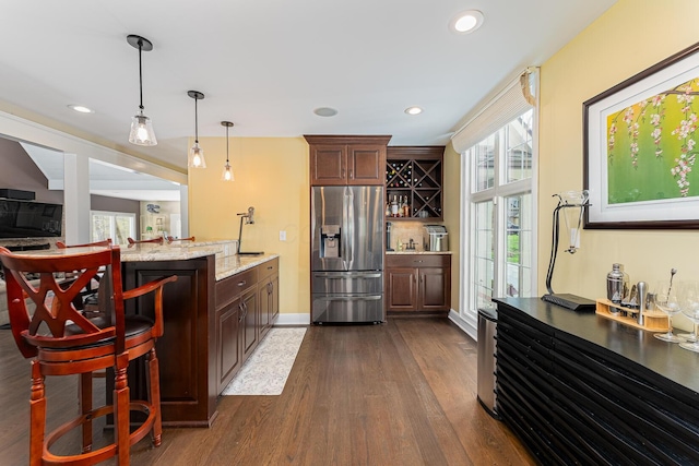kitchen with stainless steel fridge, light stone countertops, dark wood-type flooring, decorative light fixtures, and a breakfast bar area