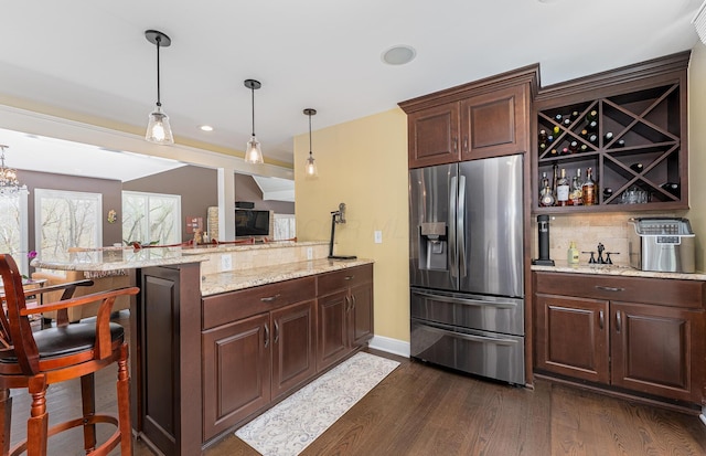 kitchen with decorative backsplash, dark wood-style flooring, a peninsula, light stone counters, and stainless steel fridge with ice dispenser