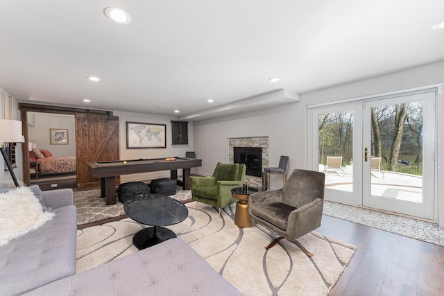 living area featuring french doors, a barn door, wood finished floors, a stone fireplace, and recessed lighting