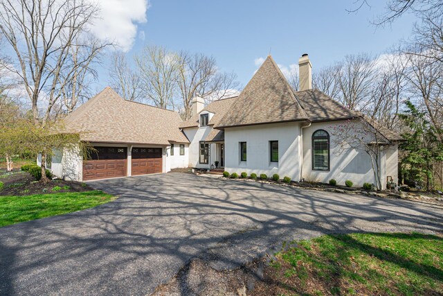 view of front of home featuring roof with shingles, a chimney, stucco siding, an attached garage, and aphalt driveway