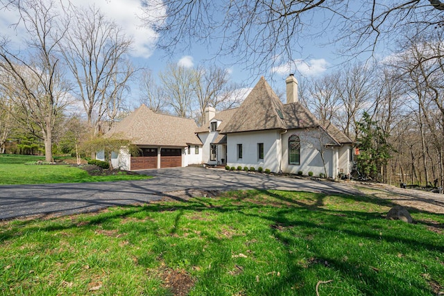 view of front of home with stucco siding, an attached garage, aphalt driveway, a front lawn, and a chimney