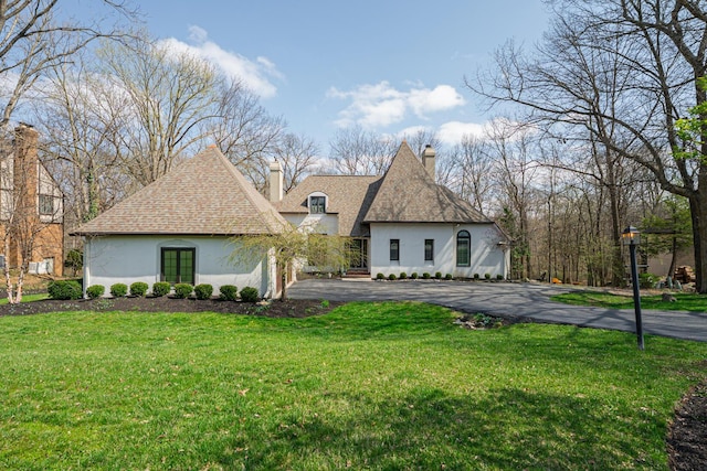 back of house featuring a chimney, a lawn, stucco siding, driveway, and a shingled roof