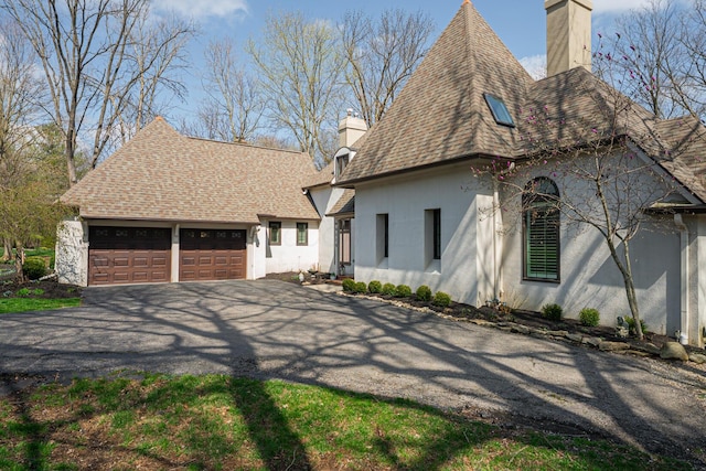 view of front of house featuring aphalt driveway, a chimney, an attached garage, and stucco siding