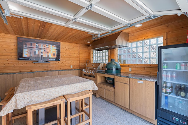 kitchen with refrigerator with glass door, wooden ceiling, dark stone counters, wooden walls, and extractor fan