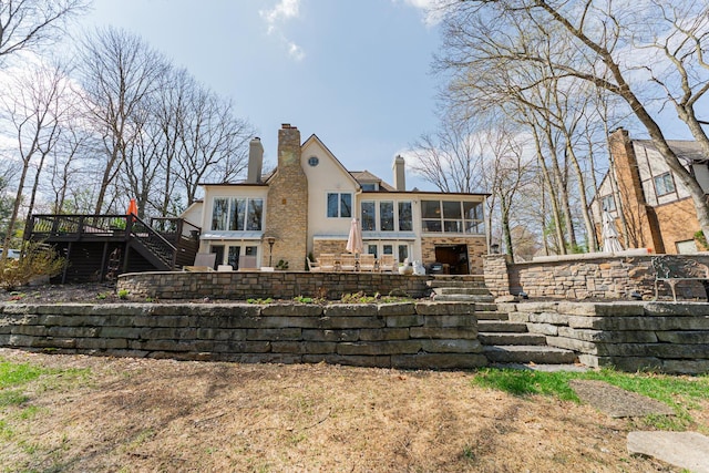 back of property featuring a sunroom, stucco siding, stairway, a deck, and a chimney