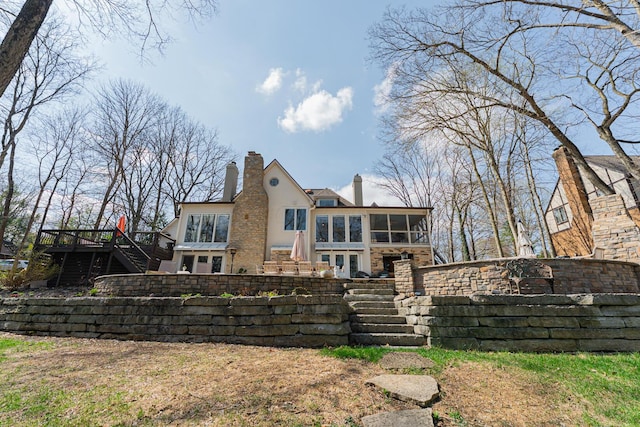 rear view of property with stucco siding, a sunroom, a chimney, and stairs
