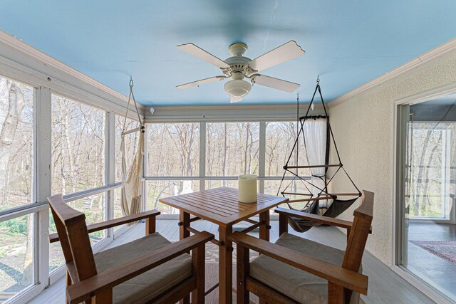 sunroom with a ceiling fan, a textured wall, crown molding, and wood finished floors