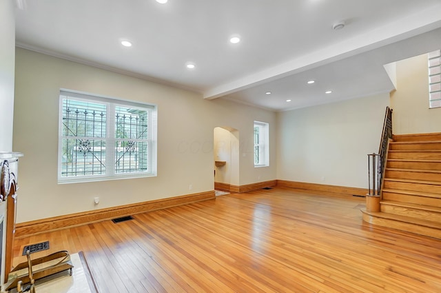unfurnished living room featuring light wood-type flooring, arched walkways, crown molding, and visible vents