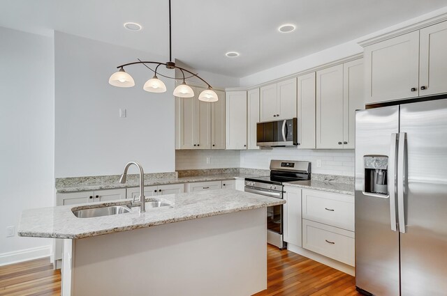kitchen featuring light wood finished floors, a kitchen island with sink, stainless steel appliances, a sink, and pendant lighting