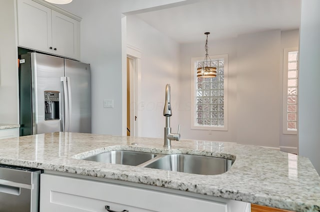 kitchen featuring a sink, stainless steel refrigerator with ice dispenser, decorative light fixtures, and light stone counters
