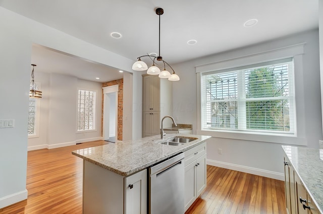 kitchen with a sink, light stone countertops, dishwasher, hanging light fixtures, and light wood-type flooring