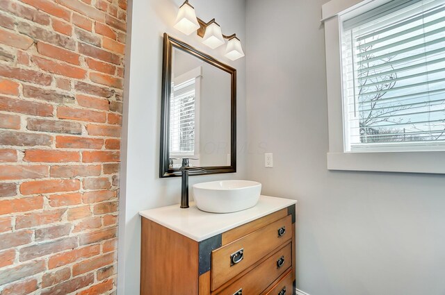 bathroom featuring vanity, brick wall, and a healthy amount of sunlight