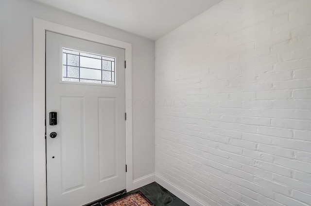 foyer entrance with baseboards and brick wall