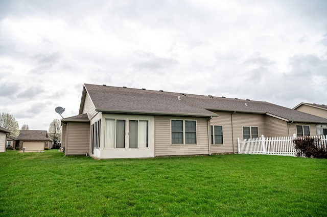 back of property with a shingled roof, fence, and a lawn