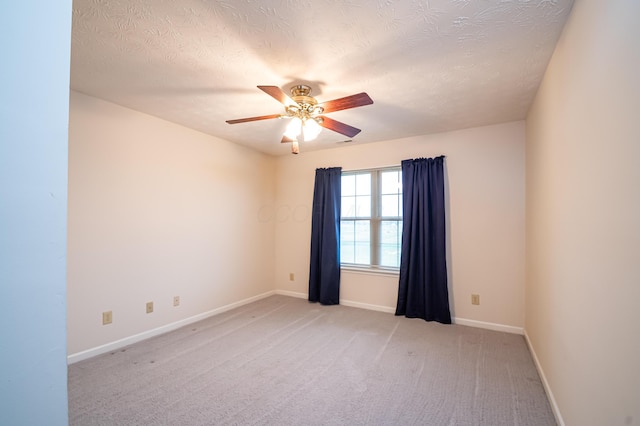 spare room featuring light colored carpet, a textured ceiling, baseboards, and a ceiling fan