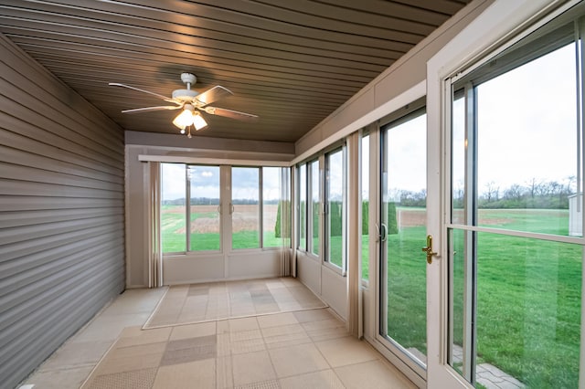 unfurnished sunroom with a ceiling fan and a rural view