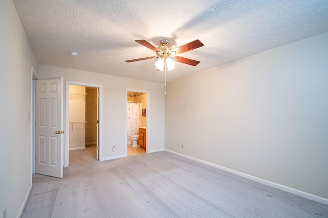 unfurnished bedroom with a walk in closet, light colored carpet, baseboards, a textured ceiling, and a closet