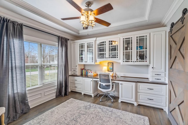 home office with built in desk, ornamental molding, dark wood-type flooring, a barn door, and ceiling fan