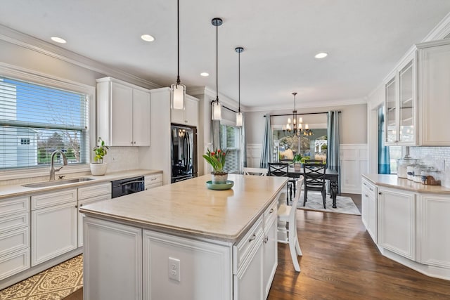 kitchen featuring light countertops, a sink, wainscoting, black appliances, and ornamental molding