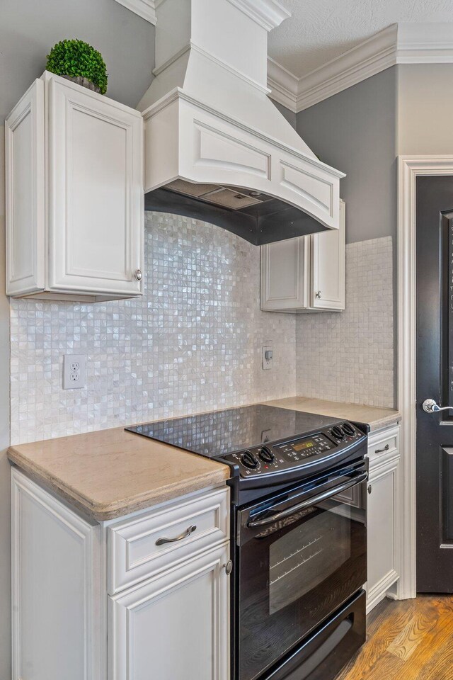 kitchen with white cabinets, ornamental molding, premium range hood, and electric range