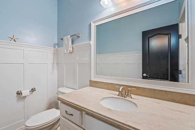 half bathroom with a wainscoted wall, toilet, a decorative wall, and vanity