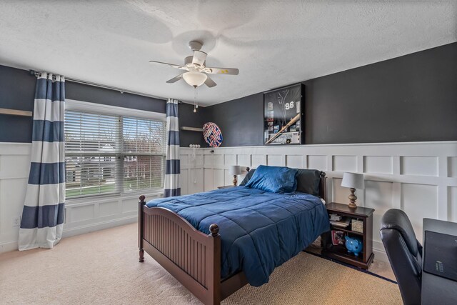 carpeted bedroom with a wainscoted wall, a textured ceiling, a decorative wall, and a ceiling fan