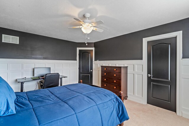 carpeted bedroom featuring a ceiling fan, wainscoting, and visible vents