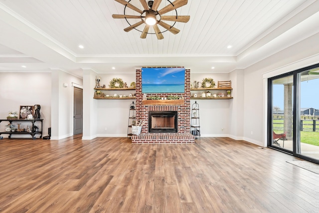 unfurnished living room featuring a ceiling fan, a fireplace, wood finished floors, baseboards, and ornamental molding
