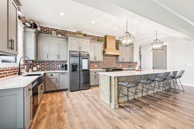 kitchen with appliances with stainless steel finishes, gray cabinets, custom exhaust hood, and a kitchen bar