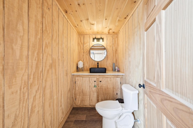 half bathroom featuring wood walls, a sink, wood finished floors, and toilet
